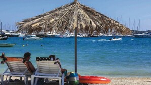 A beach scene with a thatched umbrella, two lounge chairs, and a red inflatable ring on the sand.