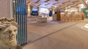 A modern hotel lobby with a seating area, a reception desk, and a large window offering a view of the outdoors.