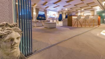 Een moderne hotellobby met een zithoek, een receptiebalie en een groot raam met uitzicht op het omliggende landschap.