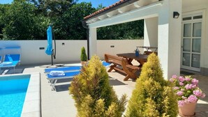 A poolside area with a table and chairs, a covered seating area, and a potted plant. - Two Bedroom Apartment With Private Pool (Privlaka)