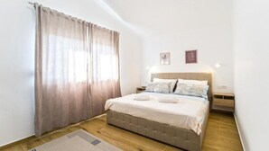 A bedroom with a bed, curtains, a nightstand, and wall art. - Two Bedroom Apartment With Private Pool (Privlaka)
