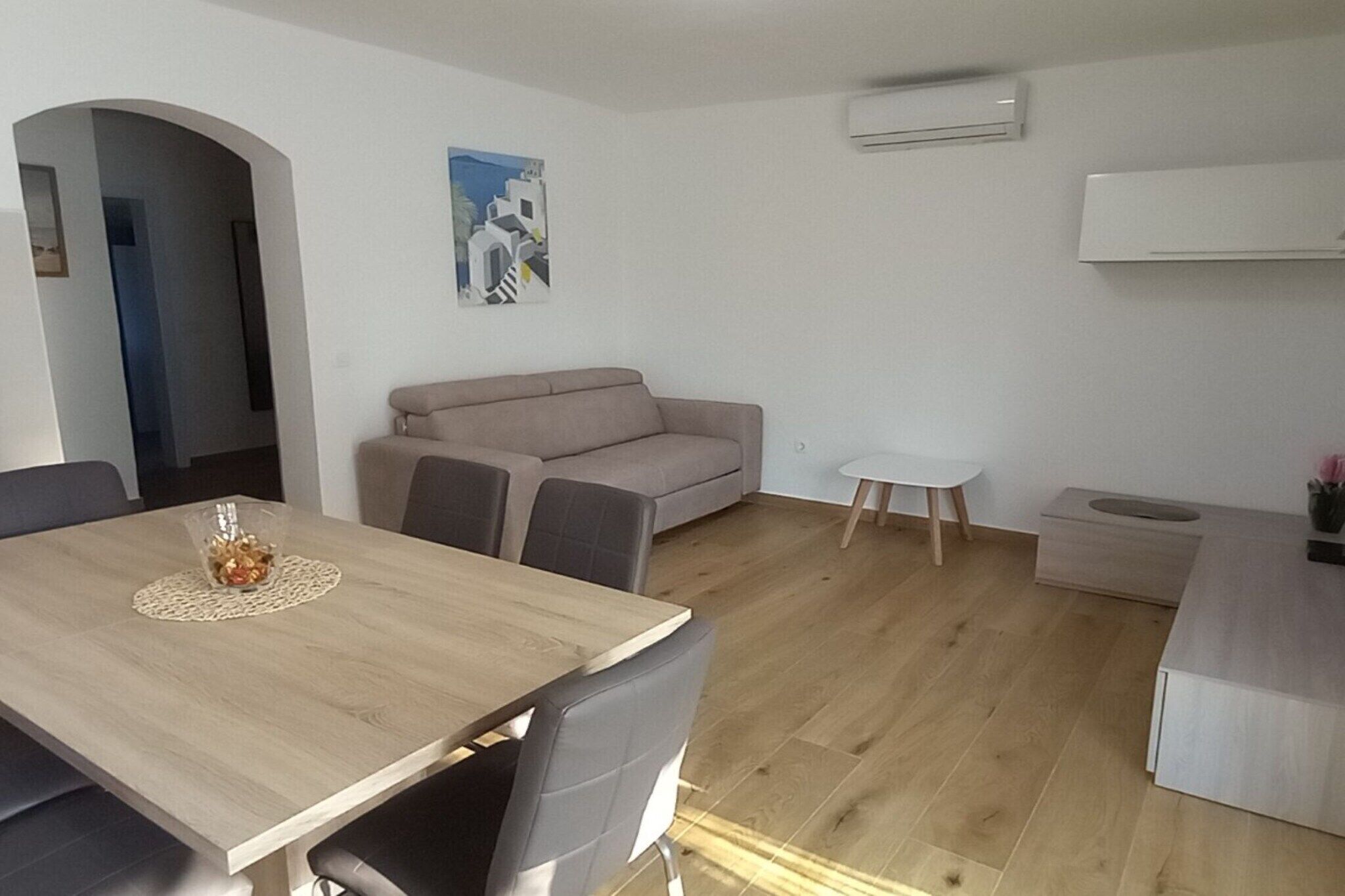 A modern living room with a wooden dining table, grey sofa, and a small white side table.