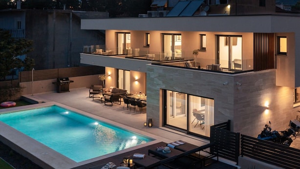 Ein modernes, zweistöckiges Haus mit Swimmingpool, Sitzgelegenheiten im Freien und großen Fenstern.