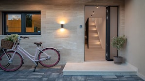Ein moderner Gebäudeeingang mit einem Fahrrad davor, einem Blumentopf und einer Treppe, die hineinführt.
