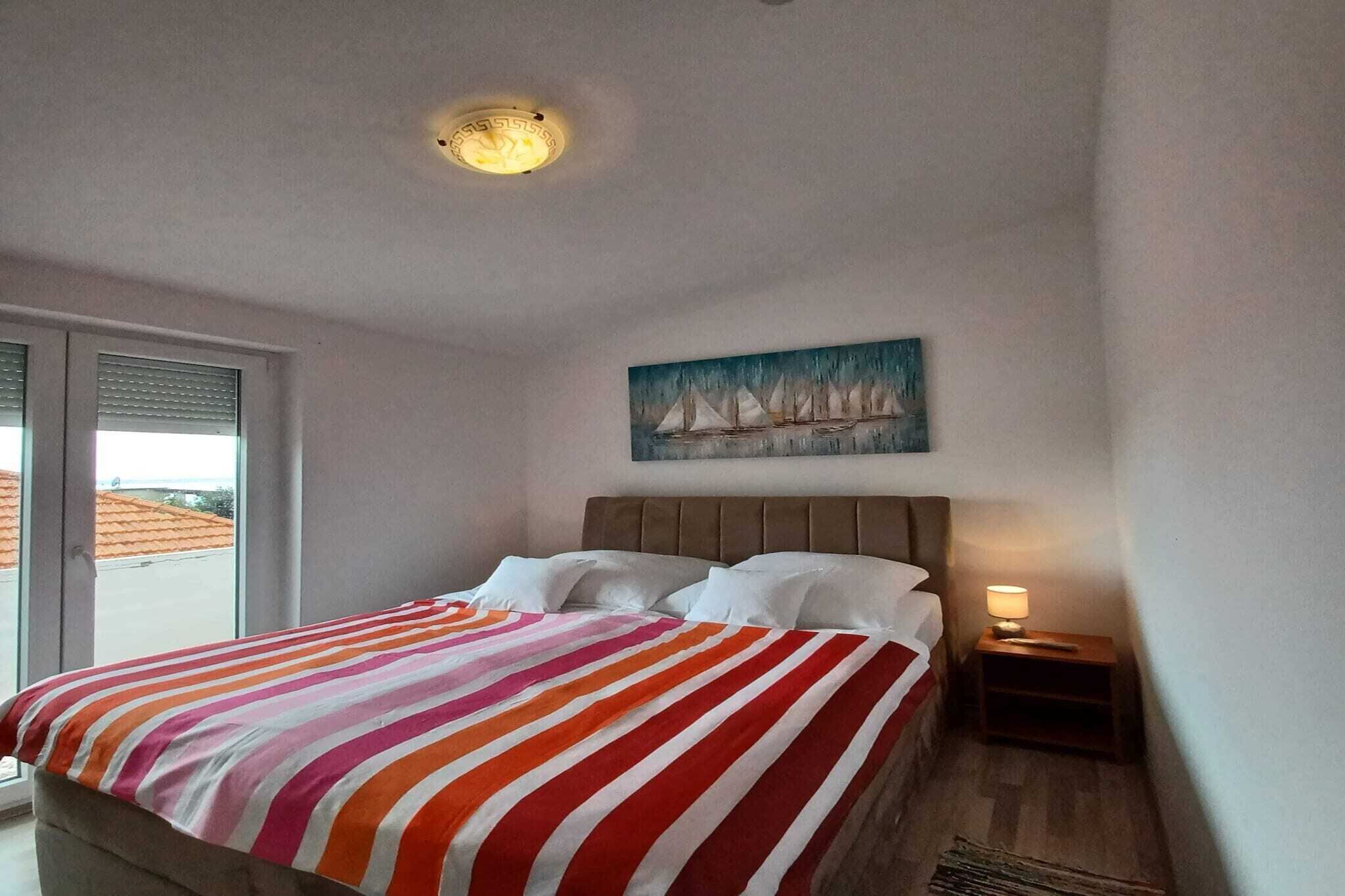 A hotel room with a bed, a painting of sailboats, a window, and a nightstand with a lamp.