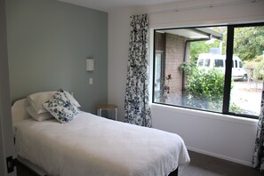 A bedroom with a bed, a small stool, a window with curtains, and a view of the outside.