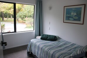 A bedroom with a single bed, a window with a view of trees, and a framed picture on the wall.
