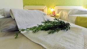 Ein ordentlich bezogenes Bett mit einem weißen Handtuch und einem Rosmarinzweig, einer Nachttischlampe und einer grünen Wand.