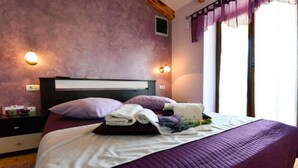 Un lit bien fait, avec une literie violette, une tête de lit et une table de chevet sur laquelle se trouve une lampe.