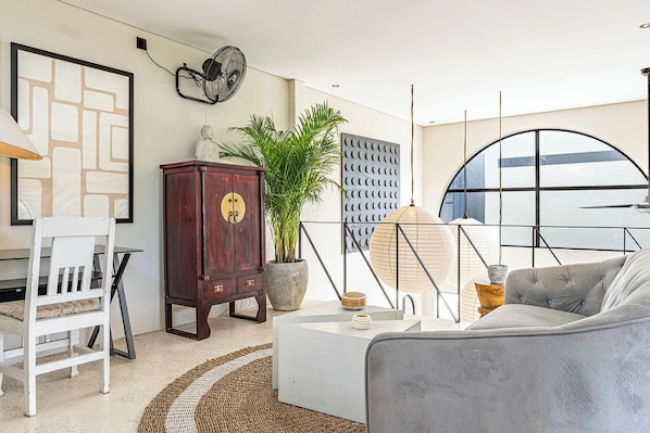 Una sala de estar moderna con un sofá blanco, un mueble de madera, una planta en maceta y un ventanal con vistas.