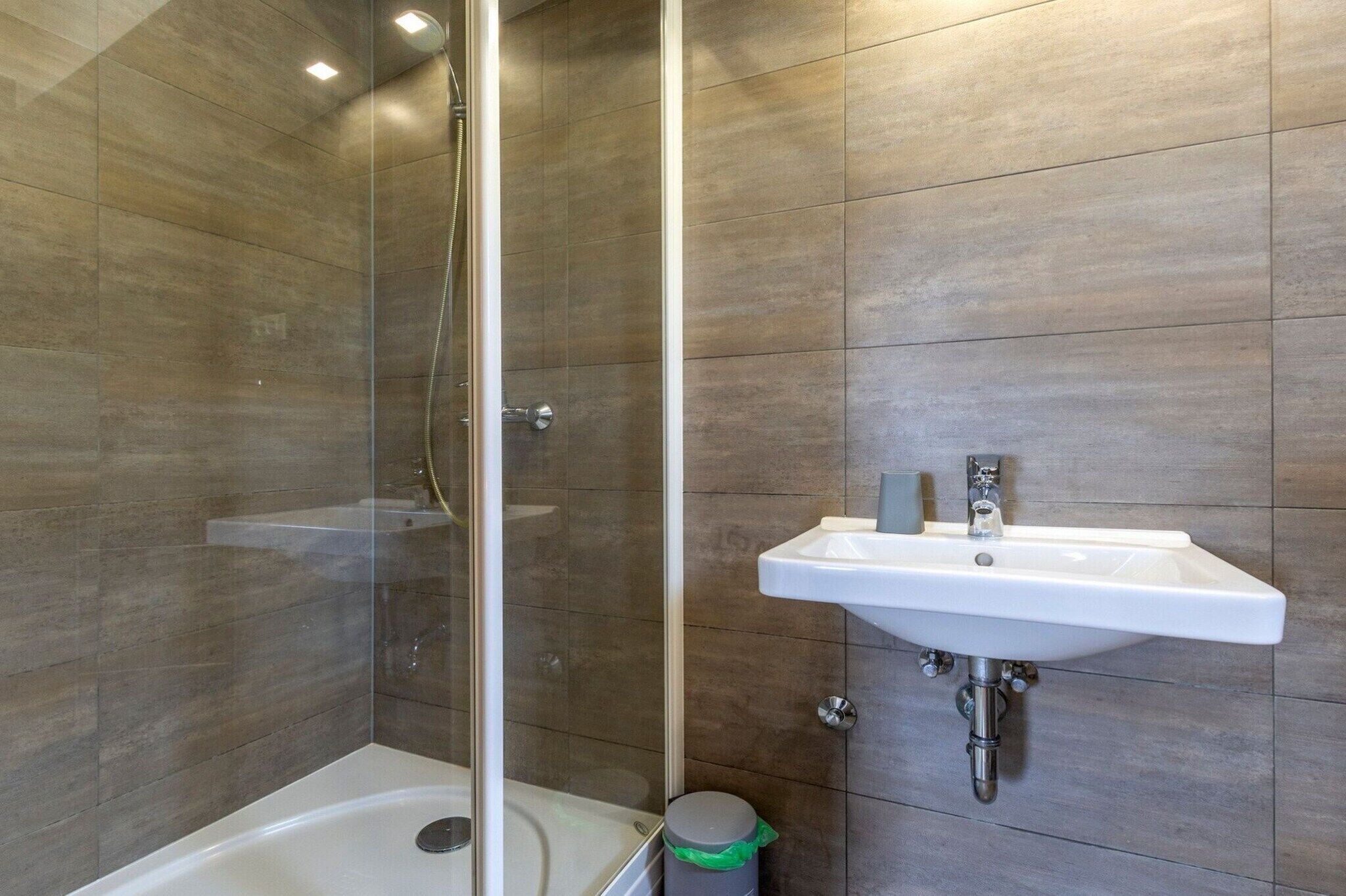 Une salle de bain moderne avec une douche à parois de verre, un lavabo blanc et une poubelle.