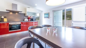 A modern kitchen with red cabinets, a large dining table, and a view of the countryside through the windows. - Serene Rural Villa with Pool, Sun Deck, and Children's Play Area - Five Bedroom Villa (Tugare)