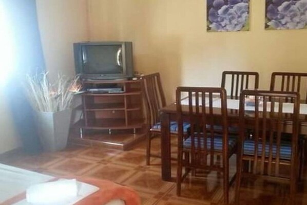 Ein Essbereich mit Holztisch und -stühlen, einem Fernseher auf einem Schrank und einer Vase mit Zweigen.