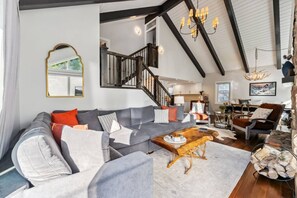 Ein geräumiges Wohnzimmer mit grauem Sofa, einem Holztisch und einer Treppe, die in eine obere Ebene führt.