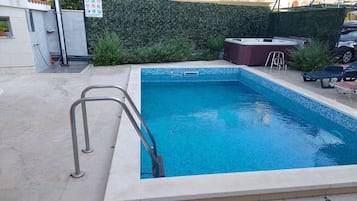 Une piscine rectangulaire avec un escalier en métal, entourée d’une terrasse en béton.