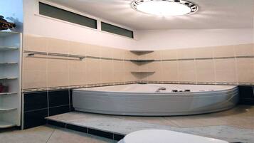Une salle de bain avec une grande baignoire, des toilettes et une étagère contenant des articles de toilette.