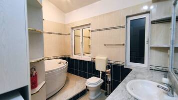 Une salle de bain équipée d’une baignoire, de toilettes et d’un lavabo, avec un sol et des murs carrelés, et un miroir au-dessus du lavabo.