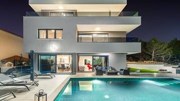 Ein modernes, zweistöckiges Haus mit Schwimmbad, Außenbereich mit Sitzgelegenheiten und Essbereich, der durch die Glastüren sichtbar ist.