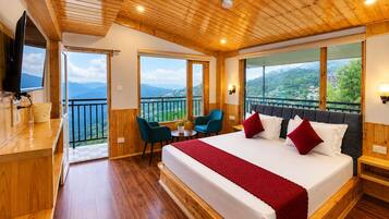 A hotel room with a large bed, a TV, a balcony with a view, and wooden flooring.