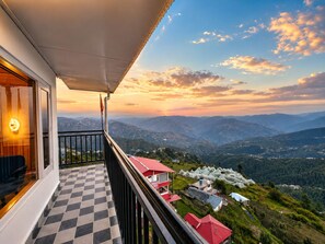 A balcony with a checkered floor, a red-roofed building, and a view of a valley with mountains. - The Kufri House (Theog)