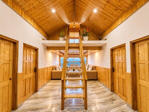 A wooden interior with a central wooden ladder, a sofa, and a view through a window. - The Kufri House (Theog)