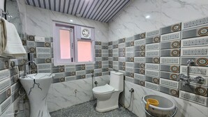 A bathroom with a white sink, toilet, and bathtub, marble walls, and a window with a pink frame. - The Kufri House (Theog)