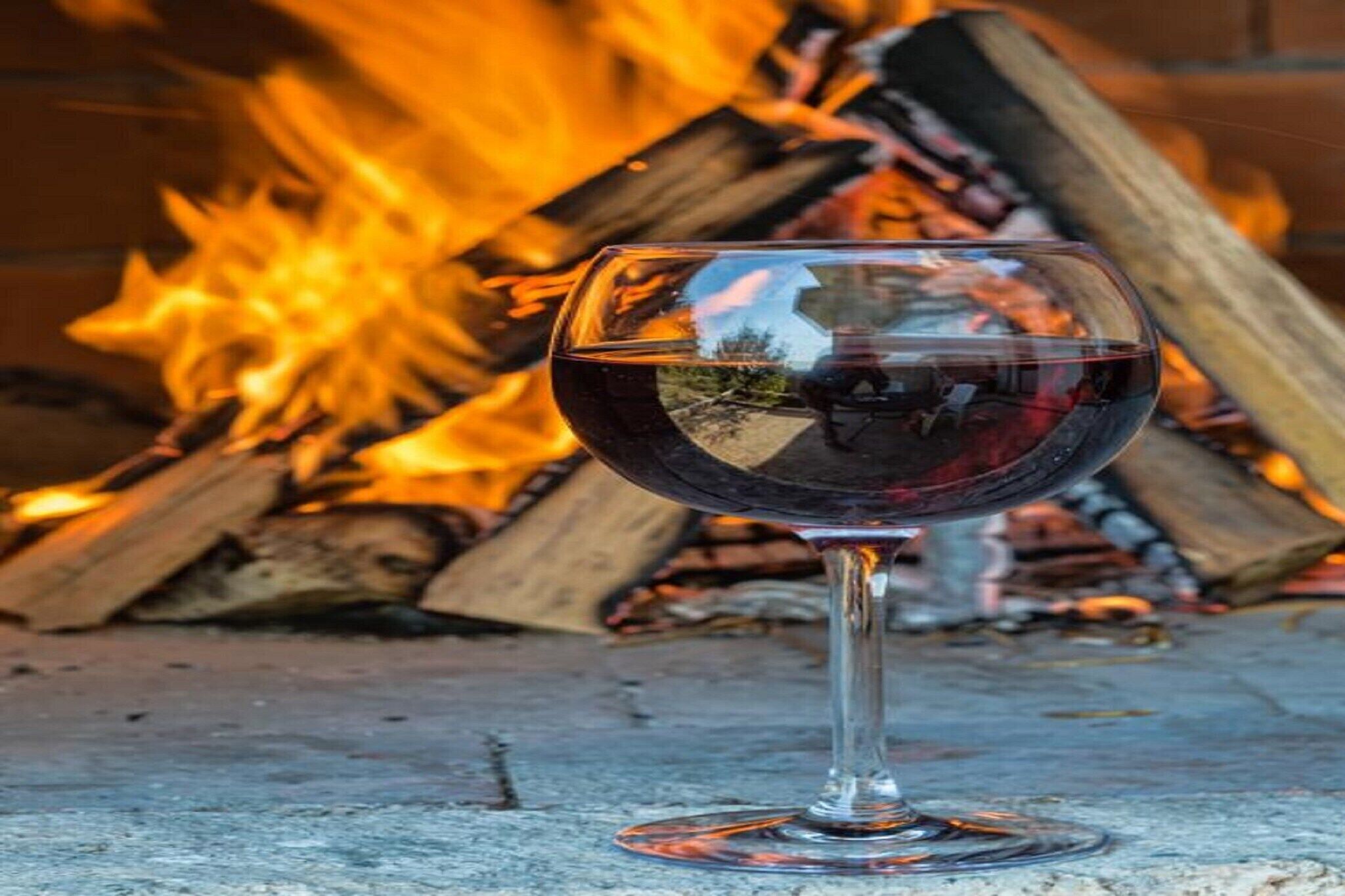 A glass of red wine in front of a fire.