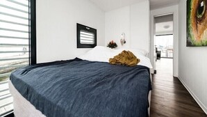 Ein modernes Schlafzimmer mit einem großen Bett, einem Fenster mit Jalousien, einer Wandleuchte und einem Gemälde.