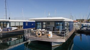 Une structure flottante moderne dotée d’un espace de détente extérieur abrité, d’une piscine et d’un quai avec des bateaux.