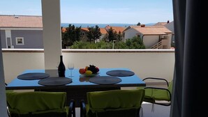 Un balcón con una mesa preparada para dos personas, una botella y un frutero.