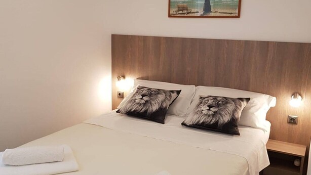 Una cama bien hecha con dos almohadas, una toalla blanca y un cuadro de una playa en la pared.