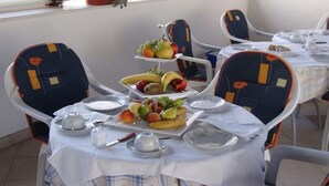 Ruokailutila, jossa on kolmikerroksinen hedelmäasetelma, valkoiset pöytäliinat ja modernit tuolit, joissa on oransseja yksityiskohtia.