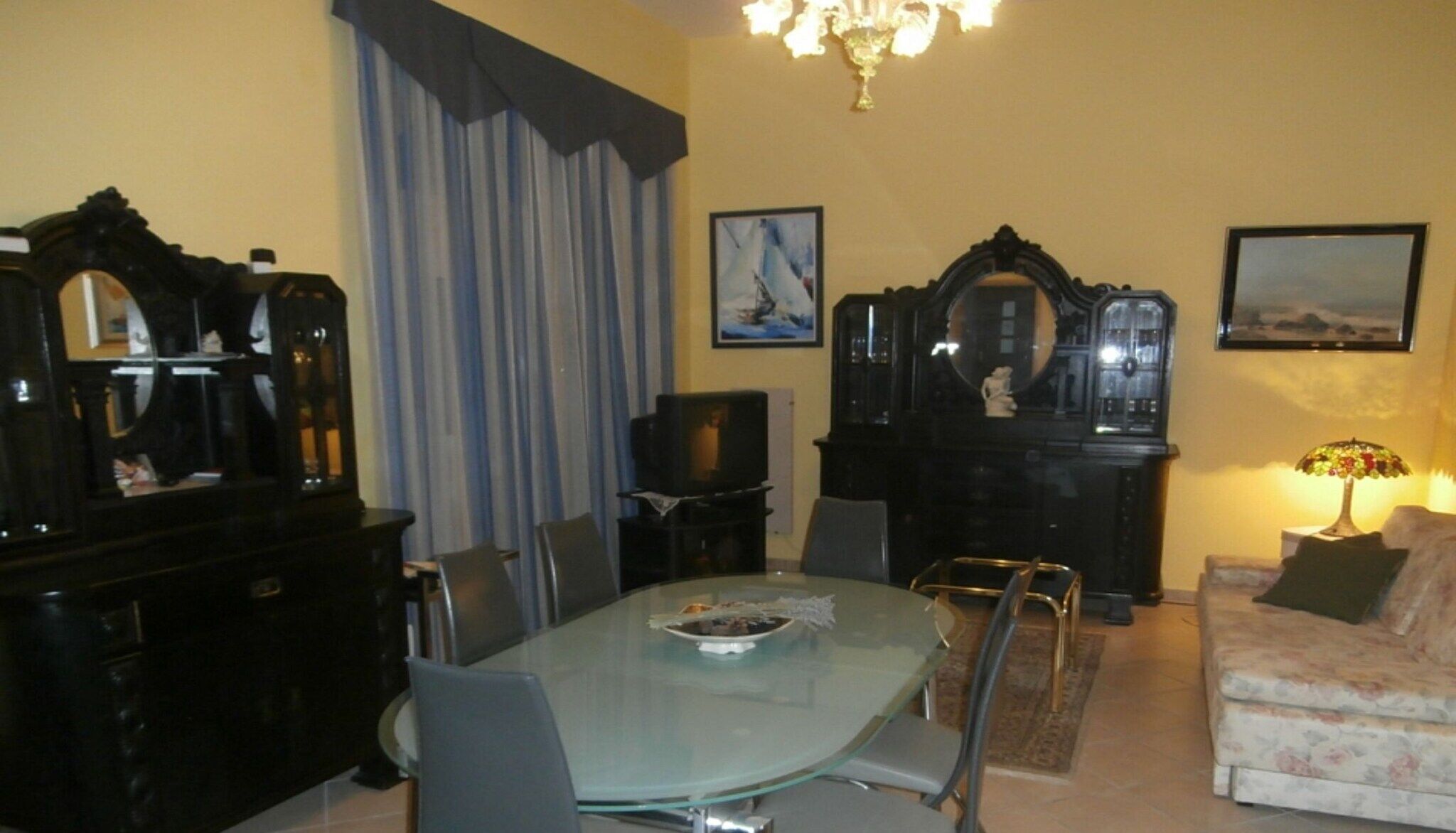 Un coin repas avec une table et des chaises en verre, un piano, un canapé et deux tableaux encadrés au mur.