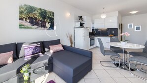 A modern living room with a sofa, a glass coffee table, and a dining area with a table and chairs. - Apartments Tafra - One Bedroom Apartment (Lokva Rogoznica)