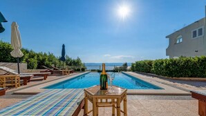 A pool area with lounge chairs and a table with a bottle and glass. - Apartments Tafra - One Bedroom Apartment (Lokva Rogoznica)