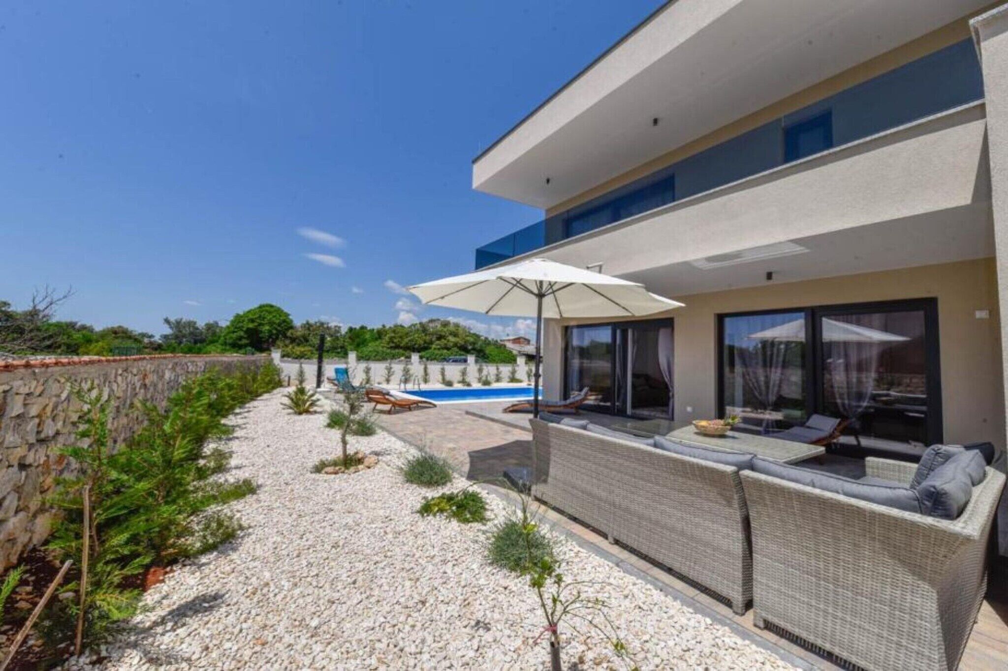 A modern house with a swimming pool, outdoor seating, and a stone wall.