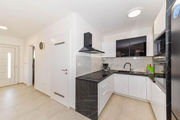 A modern kitchen with white cabinets, black countertops, and a black stove hood. - Villa Sunrise with Outdoor Pool - 4 Bedroom & Pool (Šibenik)