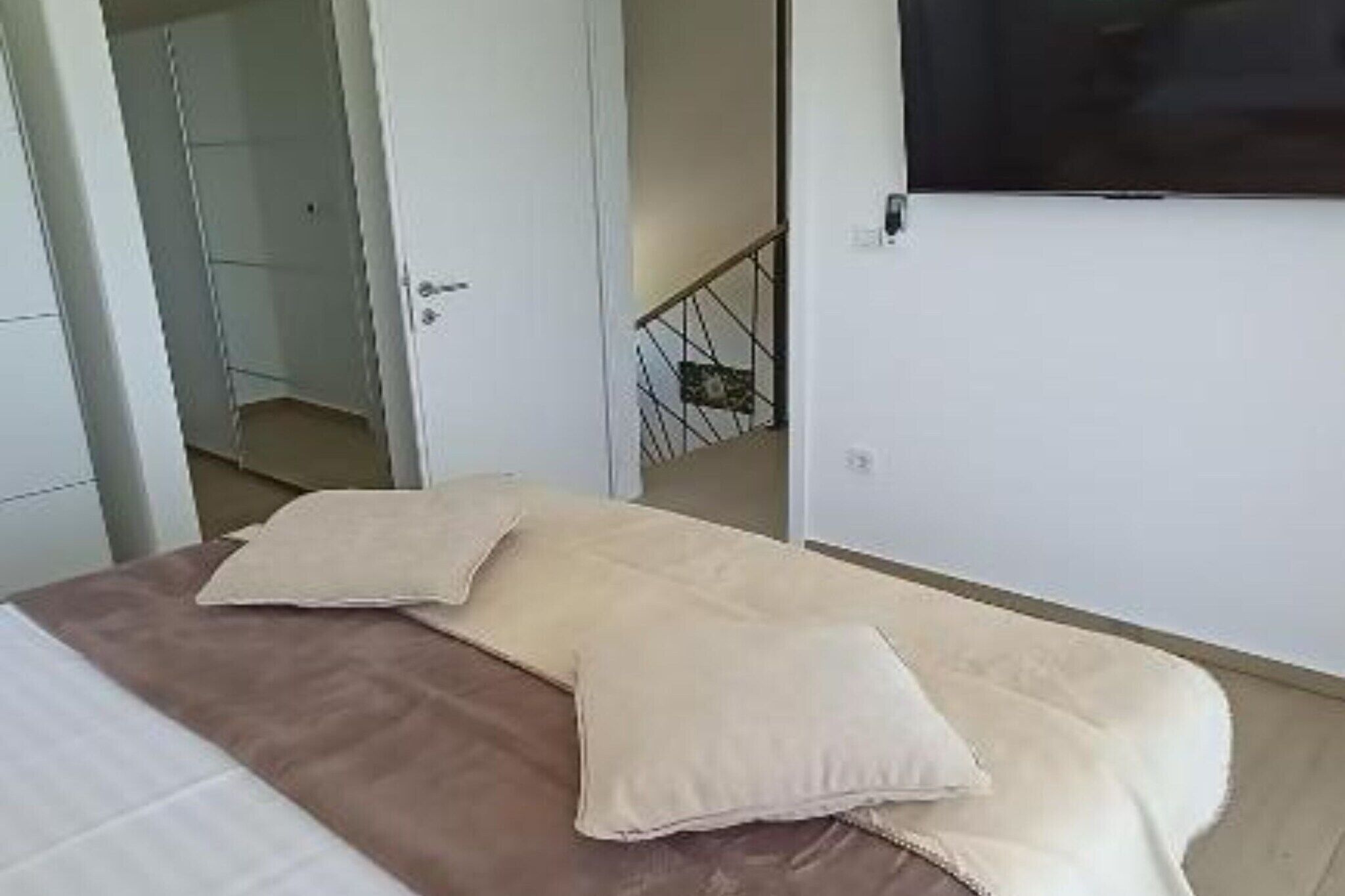 Un dormitori amb un llit, almoines, un televisor fixat a la paret i una porta que condueix a una altra habitació.