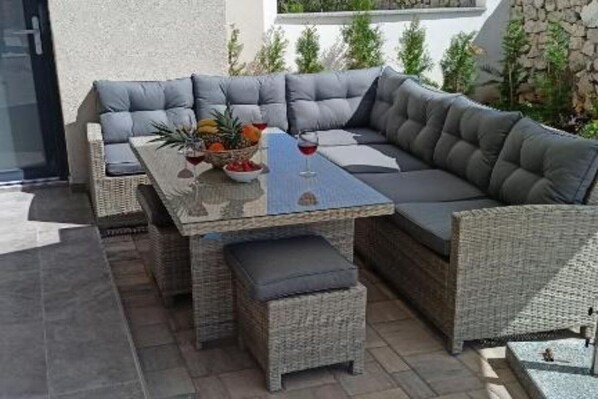 Eine Rattan-Couch mit Kissen, ein kleiner Tisch mit einer Obstschale und einem Glas Rotwein, sowie eine Bank.