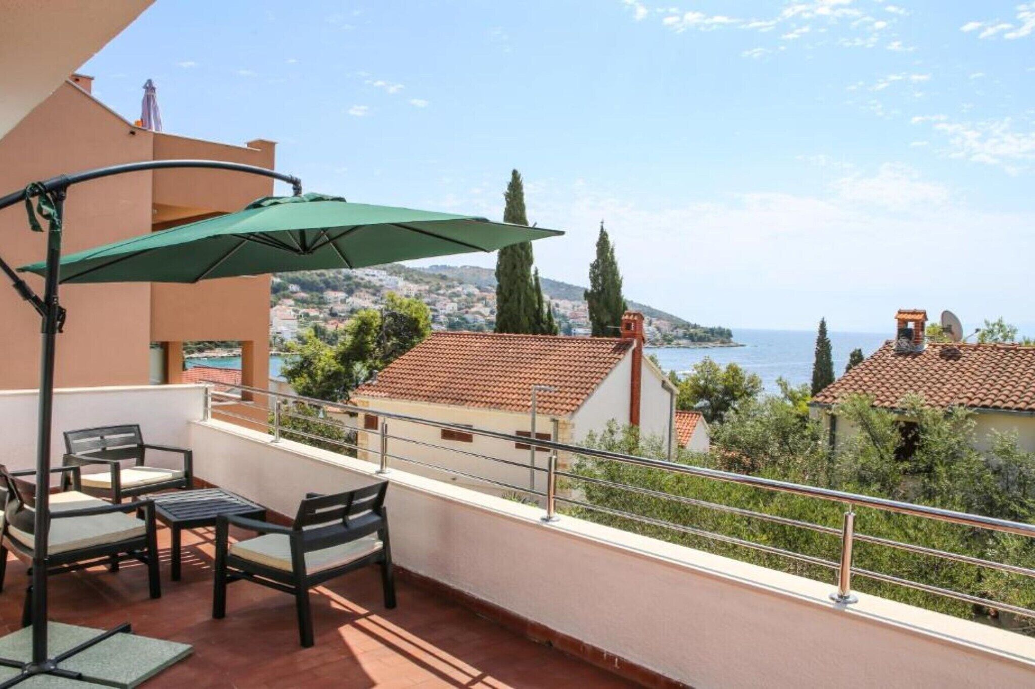 Un balcon aménagé avec du mobilier d’extérieur, un parasol vert et une vue sur la mer et les collines.