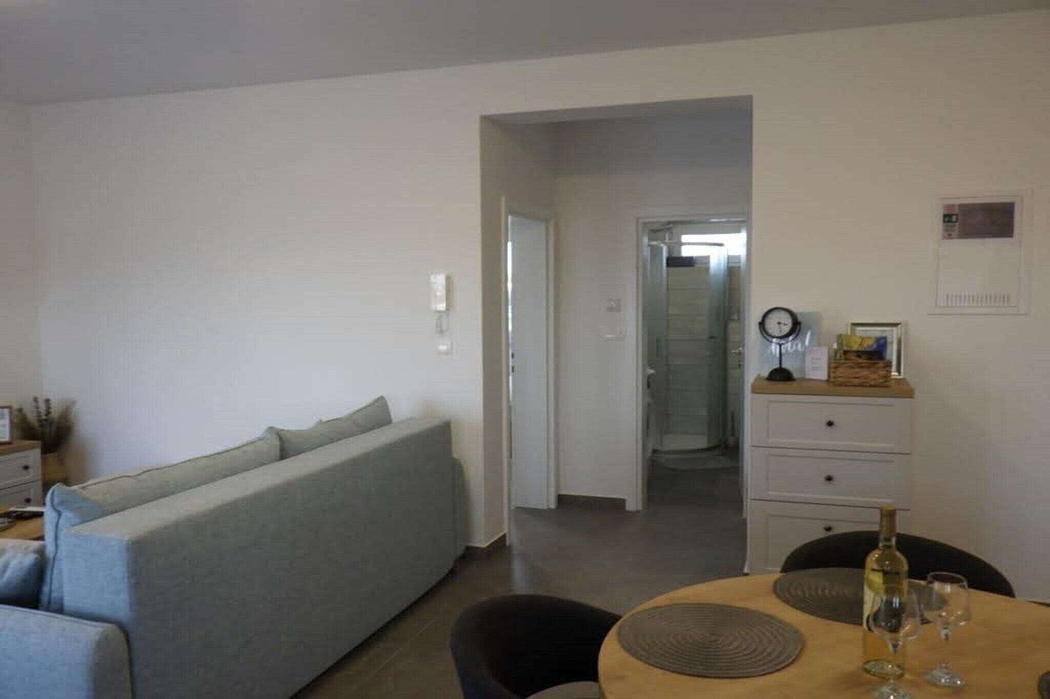 Una sala de estar moderna con un sofá gris, una mesa de comedor con copas de vino y un aparador blanco.
