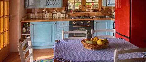 Una cocina con gabinetes azules, un refrigerador rojo y una mesa con una cesta de fruta.