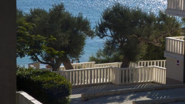 A coastal view with a white building, trees, and a clear blue sea.