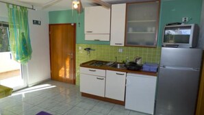 A compact kitchen with a gas stove, sink, and a refrigerator. There is a ceiling fan and a television on top of the fridge.