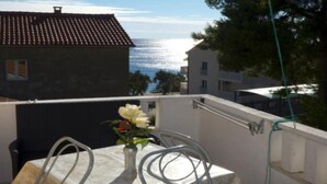 A balcony with a white table and chairs, a vase with flowers, and a view of the sea.