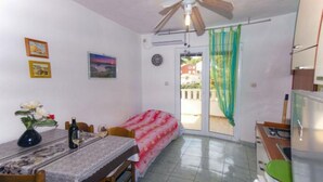 A compact room with a dining table, a bed, a ceiling fan, a kitchen area, and a sliding glass door leading to an outdoor area.