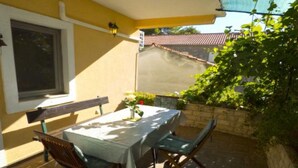 Une terrasse avec une table et des chaises, une fenêtre et une vue sur un bâtiment dont le toit est recouvert de tuiles.
