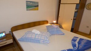 Une chambre à coucher avec un lit, des oreillers, une table de chevet, une lampe, une armoire et un tableau au mur.