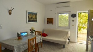 Une petite pièce agréable et chaleureuse, avec une table à manger, des chaises, un canapé, un tableau, une horloge et une fenêtre avec des stores.