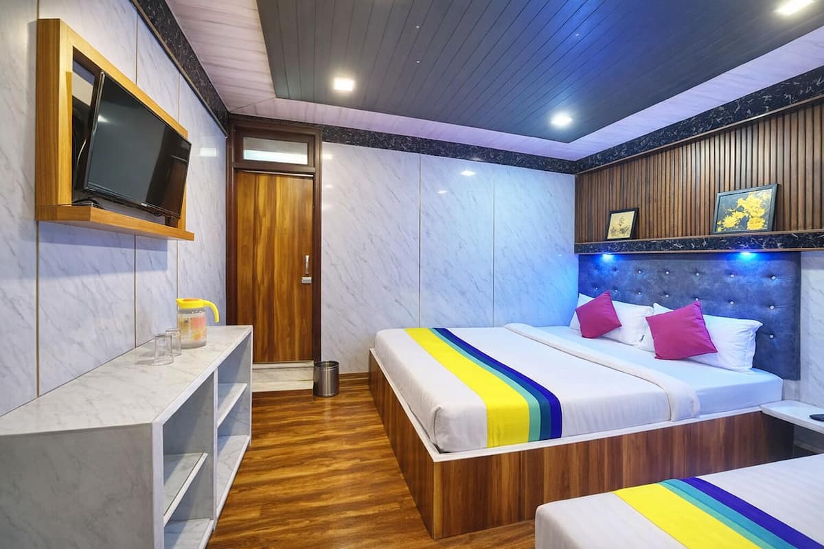 A hotel room with a bed, bedside table, TV, wooden panel wall, and a small shelf with items.